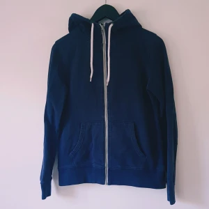 Marinblå hoodie från Race Marine strl 38 - Snygg marinblå hoodie från Race Marine, tillverkad i ekologisk bomull. Tröjan har dragkedja framtill, huva med vita snören och två stora fickor. Perfekt för chill dagar eller när du vill ha en enkel och stilren look.  Helt skick dock Ljusare i färgen & tvättludd