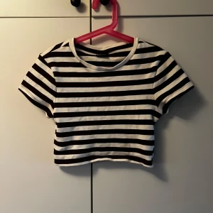 Randig croppad topp från Gina Tricot - Säljer en brun-vit randig croppad topp från Gina Tricot. T-shirten har korta ärmar, rund halsringning och är tillverkad i mjuk bomull. Väldigt croppad från vad jag minns. Katt finns i hemmet, kontakta vid fler frågor🌷