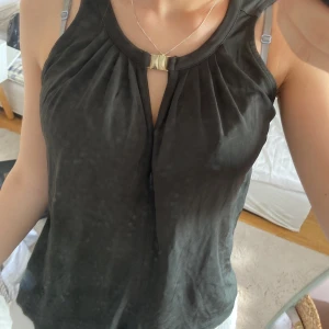 Märkgrön ärmlös topp från H&M XS - Snygg mörkgrön ärmlös topp från H&M i storlek XS. Toppen har ett elegant veckat tyg framtill och en dekorativ guldfärgad detalj vid halsringningen. Perfekt för dig som gillar stilrena och enkla plagg med en twist.
