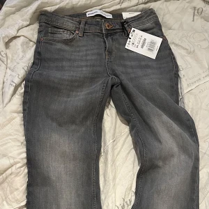 Grå jeans från Bershka - Snygga grå jeans från Bershka med klassisk femficksdesign och diskreta slitningar. Jeansen har raka ben och normal passform, perfekt för en chill och stilren look. Tillverkade i mjukt bomullsmaterial med lite stretch för extra komfort. Dom är helt nya, aldrig använt dom. Dom är i storlek 34 men är som XS/S