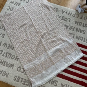Beige och vit Dior halsduk - Snygg beige och vit halsduk från Christian Dior med ikoniskt monogrammönster och fransar i kanten. Stor och lyxig, perfekt att slänga över axlarna för en classy vibe. Diskret logga längs kanterna ger extra exklusiv känsla.