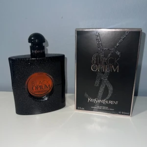 Yves Saint Laurent Black Opium EdP 90ml - Black Opium Eau de Parfum från Yves Saint Laurent i en snygg svart glittrig flaska med rund kopparfärgad detalj och tillhörande svart kartong. Flaskan rymmer 90 ml och har en modern, lyxig design som verkligen sticker ut på hyllan.