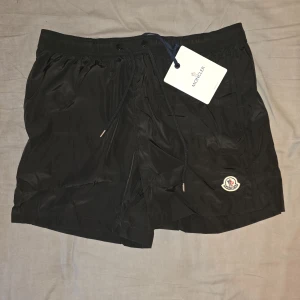 Svarta badshorts Moncler  - Svarta badshorts från Moncler med klassisk logga på benet och justerbar snörning i midjan. Fina att bada i nu till sommaren (L size)