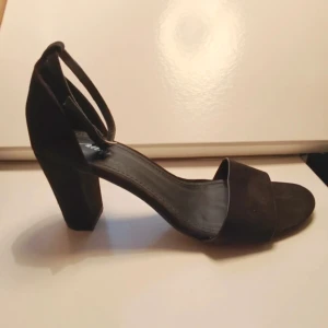 Svarta klackskor - Stilrena svarta sandaler i mocka från Alley med bred rem över tårna och justerbar rem runt ankeln. Klassisk och snygg design.