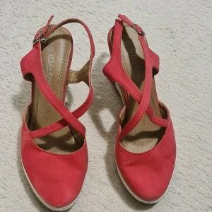 Rosa kilklack sandaler White Rose - Snygga sandaler med kilklack (9cm) från White Rose i en stark rosa färg. Skorna har korsade remmar över foten, öppen häl och justerbart spänne. Ovandelen är i textil och klacken är i kork med vit sula för en fräsch sommarkänsla.