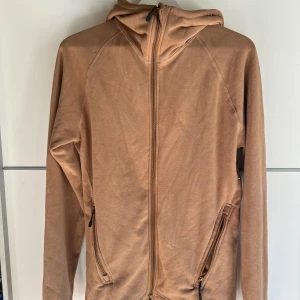 Beige hoodiejacka från 157, storlek S - Snygg beige hoodiejacka från 157 med dragkedja hela vägen och två fickor med dragkedja. Jackan har huva och är tillverkad i mjukt bomullsmaterial. Perfekt för chill dagar eller när du vill ha en enkel och clean look.