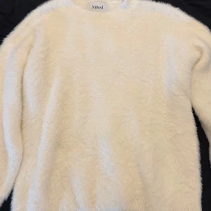 Fluffig vit tröja från Nitted - Supermjuk och fluffig vit tröja från Nitted med rund halsringning. Tröjan har lång ärm och är tillverkad i ett pälsliknande material som känns riktigt cozy. 
