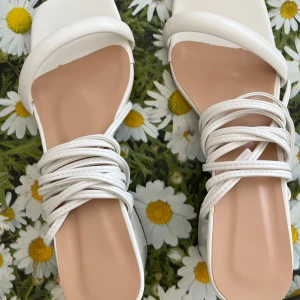 Vita sandaler med snörning och klack - Trendiga vita sandaler med fyrkantig tå, blockklack och tunna remmar som snöras runt vristen. Skorna har öppen tå och en stilren design som passar perfekt till sommarens outfits. Tillverkade i syntetmaterial med en plattformslook och låg klack.