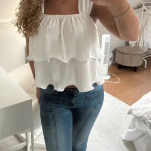 Vit volangtop från SHEIN - Superfin vit topp från SHEIN med breda axelband och dubbla volanger. Plisserad struktur och flowig passform som ger en luftig känsla. Perfekt till jeans eller kjol för en fräsch look. Säljes i storlek S.