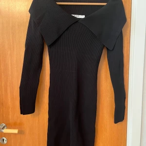 Svart ribbad klänning från NA-KD - Supersnygg svart ribbad klänning från NA-KD med bred krage som går över axlarna. Klänningen är figurnära, har lång ärm och är i stretchigt material. Perfekt till t. Ex nyår💕