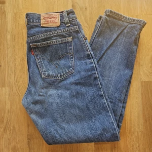 Levi's 550 Relaxed Tapered Jeans - Säljer ett par klassiska Levi's 550 Relaxed Tapered jeans i en fin blå denimtvätt. Dessa jeans är kända för sin bekväma passform med lite mer utrymme i låren och en smalare avsmalnande benslut. Jeansen är i gott begagnat skick. De är tillverkade i 100% bomull och gjorda i Mexiko. Observera att det finns lite slitage vid grenen (se bild). StorlekMidja 37cm Innerbenslängd: 77 cm W29/30 L30