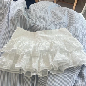 Vit volangkjol från H&M, stl 38 - Superfin vit kortkjol från H&M i storlek 38. Kjolen har flera lager volanger och broderade detaljer. Den är helt oanvänd med lappen kvar! 