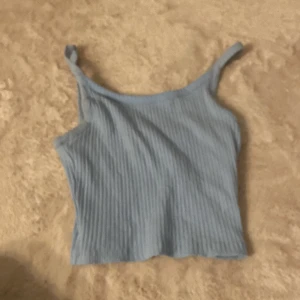 Ljusblå ribbad linnetopp FB Sister - Supersöt ljusblå ribbad linnetopp från FB Sister. Toppen har smala axelband och är croppad i modellen, perfekt till höga jeans eller kjol. Mjuk och stretchig känsla, enkel att styla för en chill look.