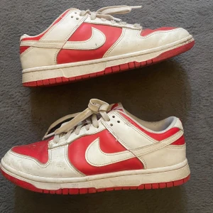 Nike Dunk Low röd/vit sneakers - Nike Dunk Low sneakers i rött och vitt skinn med klassisk låg siluett. Skorna har vit swoosh, röda paneler och vit snörning. Yttersulan är röd och ovandelen har perforeringar på tån för extra ventilation. Slutsåld modell som ej går att få tag i längre, perfekt för dig som gillar retrovibbar och streetstyle. Storlek 41, nypris 3999kr och jag säljer dem för 1899kr. Skriv om du är intresserad!😃