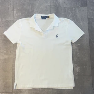 Vit pikétröja från Polo Ralph Lauren - Klassisk vit pikétröja från Polo Ralph Lauren i bomull. Tröjan har korta ärmar, krage och den ikoniska broderade loggan på bröstet. Perfekt för en clean och stilren look. Classic fit-modell som passar till det mesta. Är i storlek M men passar mer åt S 