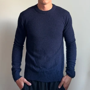 Mörkblå stickad tröja herr - En enkel och stilren mörkblå stickad tröja med rund halsringning och ribbade muddar vid ärmslut och nederkant. Perfekt för lager-på-lager och funkar till både jeans och chinos. Klassisk passform och långärmad modell.