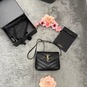 Svart quiltad axelväska från Saint Laurent - Säljer en svart quiltad axelväska från Saint Laurent med ikoniskt YSL-emblem i guld framtill. Väskan är tillverkad i skinn och har justerbar axelrem samt guldfärgade metalldetaljer. Invändigt finns flera fack och en dragkedja för extra förvaring.Finns spår av användning inuti från smink(puder fläckar) men annars hel & ren utvändigt 🥰 köpt i 2:a hand här på Plick… därav pris😃