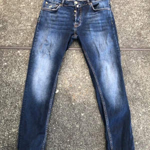 Steve Satin Jeans blå jeans 32/32 - Snygga blå jeans från Steve Satin Jeans i storlek 32/32. Klassisk femficksmodell med guldfärgad brodyr på myntfickan och kontrastsömmar. Jeansen har en rak passform och är tillverkade i slitstarkt denimtyg. Perfekta för en avslappnad och cool stil.Slitage enl bilder på fram fickorna, annars riktigt bra skick, sparsamt använda.