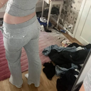 Grå mjukisbyxor Juicy Couture - Säljer ett par grå mjukisbyxor från Juicy Couture med broderad logga på benet och snörning i midjan. Byxorna har raka ben, fickor med lock och silverfärgade detaljer. Perfekta för chill dagar och riktigt sköna att ha på sig.