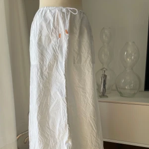 Vit långkjol från Miss Sixty - Vit långkjol från Miss Sixty med rak passform och dragsko i midjan. Kjolen är tillverkad i ett tunt bomullstyg och har en enkel, stilren look med diskreta sömdetaljer. Perfekt för en chill och clean stil. Reglerbar midja men max 86 cm