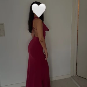 Vinröd långklänning med öppen rygg - Säljer en vinröd långklänning med smickrande passform och öppen rygg. Klänningen har smala axelband, v-ringning och ett elegant fall. Perfekt för bal eller festliga tillfällen. Materialet känns mjukt och följsamt mot kroppen.