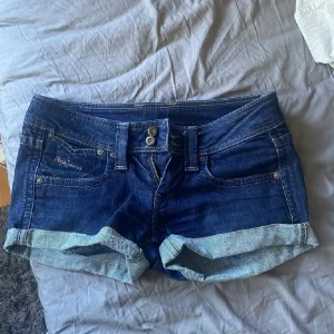 Lågmidjade jeansshorts - Snygga mörkblå jeansshorts från Pepe Jeans med uppvikta benslut och klassiska fem fickor. Shortsen har dubbla knappar och dragkedja framtill samt broderad logga på fickan. Perfekta för sommardagar och enkel att matcha med allt. Skriv om ni har några frågor eller något💞Jag säljer dem för att dem är tyvärr för stora💞Midjemåttet är ca 38/39 och priset kan alltid diskuteras!! 