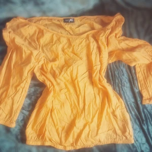 Gul offshoulder blus från JC - Snygg gul blus från JC med offshoulder-modell och långa ärmar. Toppen har resår vid ärmslut och nederkant för en skön passform. Perfekt för dig som vill ha en färgstark och trendig look.