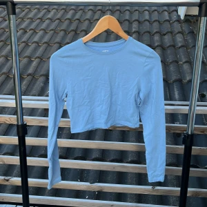 Ljusblå croppad långärmad topp 157 - Ljusblå croppad långärmad topp från 157. Enkel och stilren design med rund halsringning. Tillverkad i mjuk bomull med lite stretch för en skön passform. Perfekt att matcha med höga jeans eller kjol för en chill look.