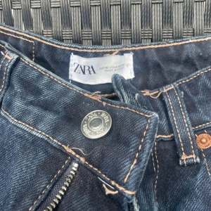 Mörkblå bootcut jeans från Zara - Mörkblå jeans från Zara med bootcut passform och råa, fransiga benslut. Klassisk femficksmodell med kontrastsömmar och dragkedja. Perfekta för dig som gillar en retrovibe och vill ha ett par jeans med lite extra attityd.