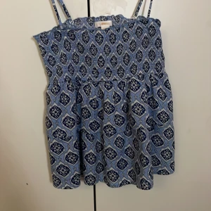 Blå mönstrat linne Gina Tricot - Supersöt från Gina Tricot med smala axelband och ett snyggt mönster i vitt och mörkblått. Använt 1 gång. Linnet har smock upptill och är luftig och perfekt för varma dagar. Passar dig som gillar en chill och somrig stil. Den har avtagbara axelband så kan även användas som kjol och tubtopp 