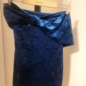 Blå sammetsklänning med rosett - Supersnygg mörkblå sammetsklänning från Soyaconcept med stor rosett upptill. Klänningen har en elegant axelbandslös design och är perfekt för dig som vill sticka ut. Mjuk och lyxig känsla tack vare sammetstyget.