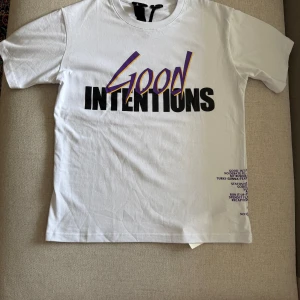 Vit Vlone Good Intentions t-shirt - Vit t-shirt från Vlone med stor svart och lila 'Good Intentions'-text på framsidan och en stor lila V. Perfekt för sommar fits och har den även i svart. Storlek S