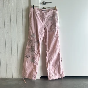 Rosa cargopants River Island - Ascoola ljusrosa cargopants från River Island med broderade blommor och pärldetaljer på benet. Byxorna har stora fickor på sidorna och snörning vid benslut.  Strlk, 10 eu, men jag är s och 165 sitter perfekt i midjan med en lite relaxed fit. Lappen kvar, aldrig använda.