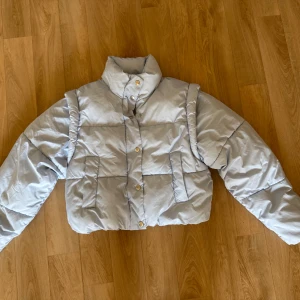 Ljusblå pufferjacka från Gina Tricot - Säljer en ljusblå pufferjacka från Gina Tricot i storlek XS. Jackan har hög krage, knappar framtill och är quiltad för extra värme. Perfekt för kyliga dagar och har en riktigt trendig, boxig passform. Materialet är polyester och jackan är långärmad.