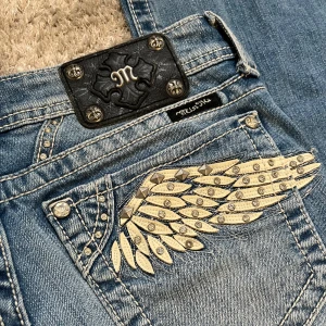 Miss Me jeans med vingar och nitar - Blå jeans från Miss Me med snygga broderade vingar och nitar på bakfickorna. Jeansen har bootcut-modell, kontrastsömmar och coola detaljer i silver. Köpta sekondhand men helt oanvända av mig🤗