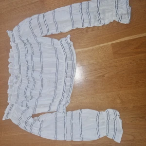 Randig offshoulder topp från H&M - Superfin vit offshoulder topp från H&M med blå ränder och långa puffiga ärmar. Toppen har resår vid axlar, ärmslut och midja för en snygg passform. Perfekt för dig som gillar en luftig och trendig stil.