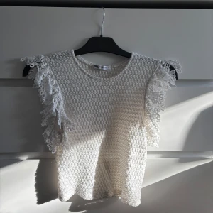 Vit spetsblus från Zara - Säljer en söt vit blus från Zara med spetsdetaljer på ärmarna. Blusen har en fin struktur och korta ärmar med volang. Hör av dig vid intresse 🤗