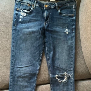 Blå jeans med slitningar - Snygga blå jeans med fabriksgjorda slitningar. De har en klassisk femficksdesign och en rak passform som ger en avslappnad look. Perfekta för en casual stil. Skinny, low waste. Storlek 30/32