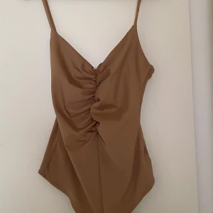 Beige body från H&M - Snygg beige body från H&M med smala axelband och rynkdetalj framtill. Perfekt för en stilren look.