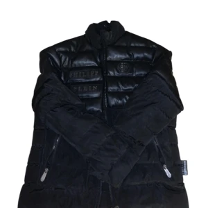 Svart pufferjacka från Philipp Plein - Snygg svart pufferjacka från Philipp Plein med dragkedja och broderade detaljer. Jackan har långa ärmar och en quiltad design som ger en cool look. Perfekt för kyligare dagar. Väldigt fin jacka. Finns ett hål inne i jackan som man ser på sista bilden därav det billiga priset. Går att diskutera pris