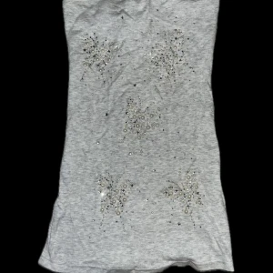 Grå tubtopp med spetsdetaljer - Snygg grå tubtopp med glittrande detaljer och spets på baksidan. Perfekt för en stilren look med en touch av elegans. Passar bra till både jeans och kjol.