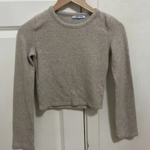 Beige croppad tröja från Zara - Säljer en beige croppad tröja från Zara Trafaluc. Tröjan har långa ärmar och är tillverkad i ett mjukt material. Perfekt för en avslappnad stil. Passar bra till jeans eller kjol. Har en liten hål fast man kan sticka den fast jätte kön in sidan och jaäät fin😍❤️