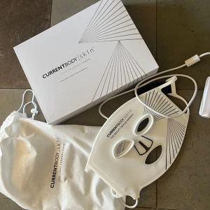 LED-mask från CurrentBody Skin - Säljer en LED-mask från CurrentBody Skin, perfekt för hudvård. Masken är vit och kommer med en förvaringspåse och laddningskabel. Den är designad för att passa ansiktet och har justerbara remmar för bekväm användning. I mycket fint skick. Nypris 3 889:- 