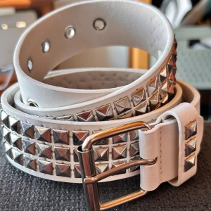 Nitbälte vintage/Y2K! - Vitt 3-radigt nibälte i vintage/Y2K-stil med pyramidnitar. Mått: L: 110 cm (80-95 cm innersta och yttersta hålet). B: 4 cm. Nytt!