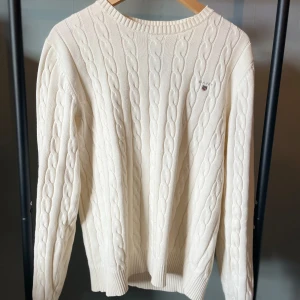 Vit kabelstickad tröja från GANT - Säljer en stilren vit kabelstickad tröja från GANT. Storlek M men passar mer som L. Tröjan är knappt använd och är i väldigt bra skick förutom lappen som håller på att ramla av 