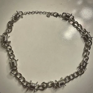 Silverfärgat halsband med taggtrådsdetaljer - Unikt silverfärgat halsband med taggtrådsinspirerade detaljer. Kedjan har en robust design med flera små länkar och justerbart lås för perfekt passform. Perfekt för att ge en edgy touch till din stil. Inte äkta silver!