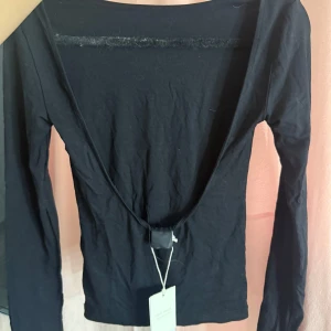 Svart långärmad topp - Säljer en stilren svart långärmad topp med djup urringning i ryggen. Perfekt för en elegant och minimalistisk look. Toppen är tillverkad i ett mjukt och bekvämt material.
