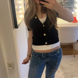 Svart ribbad kofta med guldknappar - Säljer en snygg svart ribbad kofta med guldknappar. Koftan är croppad och har en stilren design som passar perfekt till jeans eller kjol. Perfekt för en trendig look!