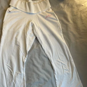 Vita mjukisbyxor från Tommy Hilfiger - Säljer ett par lågmidjade vita mjukisbyxor från Tommy Hilfiger med broderad logga i rosa på sidan. Byxorna har en bred midja och är tillverkade i mjukt material för extra komfort. Perfekta för en avslappnad stil.