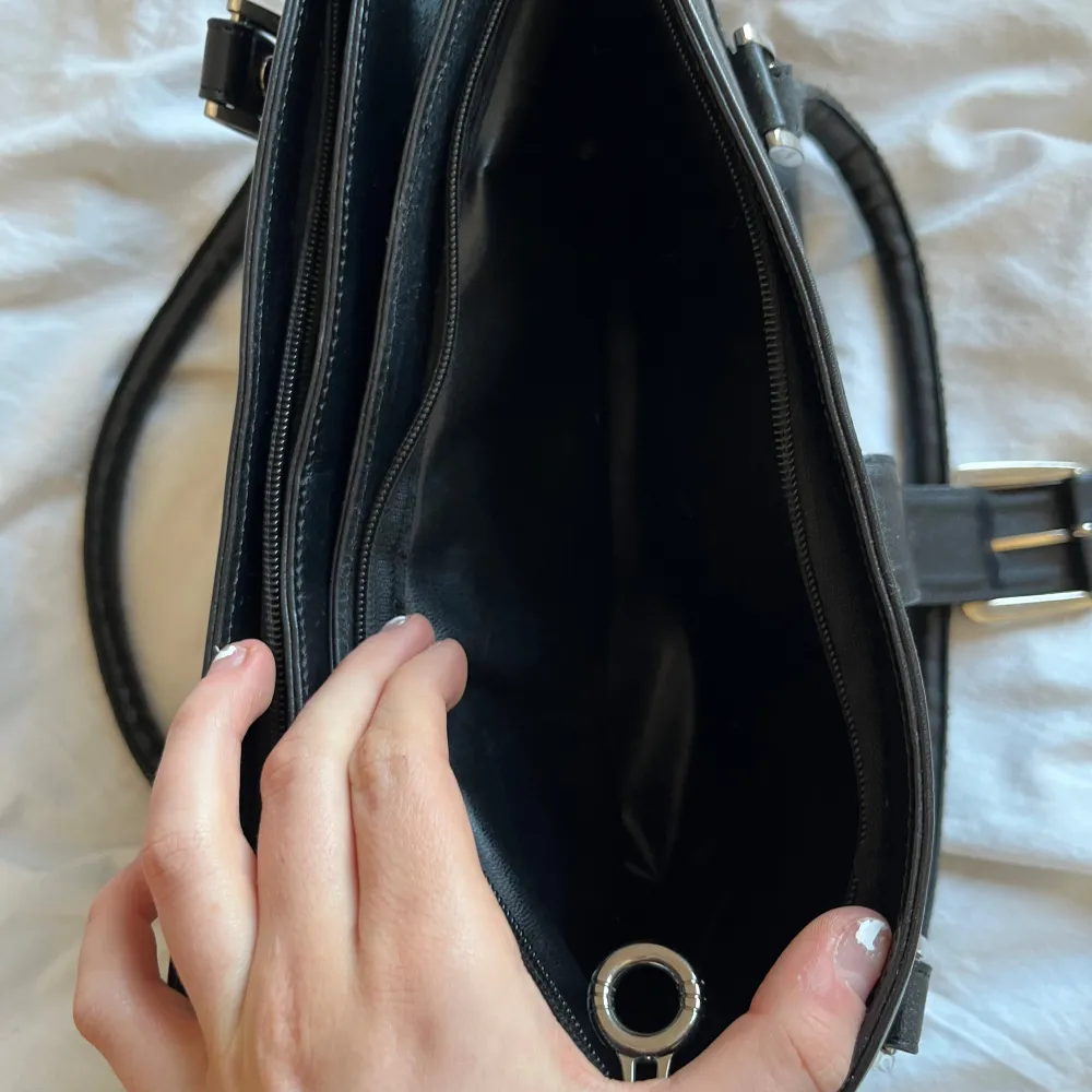 Elegant svart handväska i skinn från House of Couture. Väskan har dubbla handtag och en dekorativ spänndetalj framtill. Den är utrustad med dragkedja för säker förvaring av dina tillhörigheter. Perfekt för en stilren look. Så himla snygg! Priset kan diskuteras!!❤️💞. Laukut & Käsilaukut.